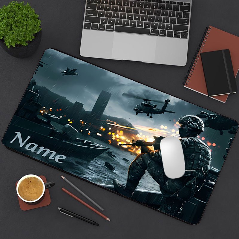 Tappetino per scrivania Deskzone™ AeroForce che raffigura una scena di battaglia notturna con un soldato in azione, elicotteri in volo e esplosioni. Il tappetino è integrato in una postazione di lavoro ordinata con una tastiera chiara, un blocco note e una pianta.