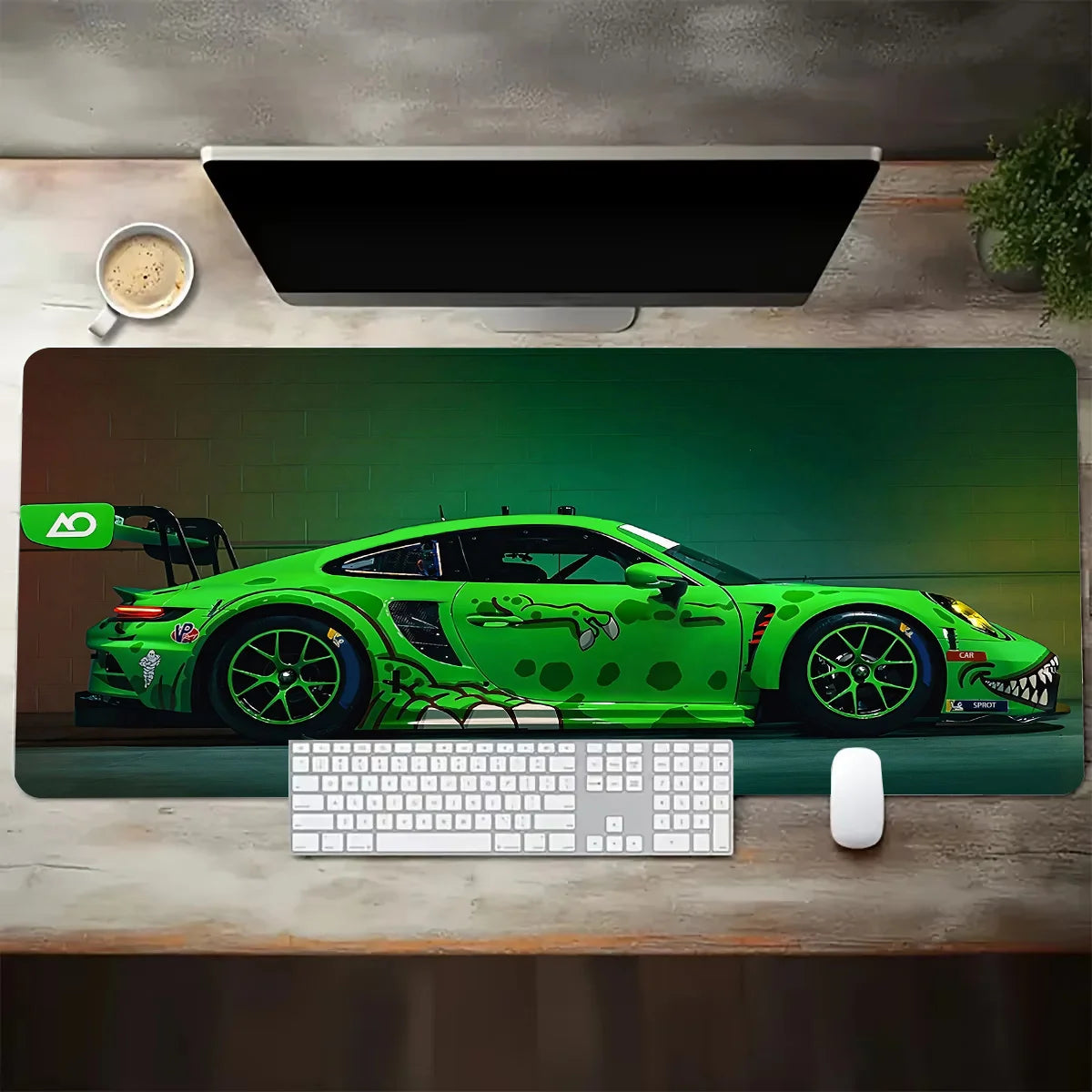 Vista dall'alto di un tappetino da scrivania esteso con il profilo laterale di un'auto da corsa sportiva verde brillante (stile Porsche) e una livrea aggressiva a tema mostro o rettile. Una tastiera bianca e un mouse sono posizionati sul tappetino, parte di un setup da scrivania con monitor, tazza di caffè e pianta.
